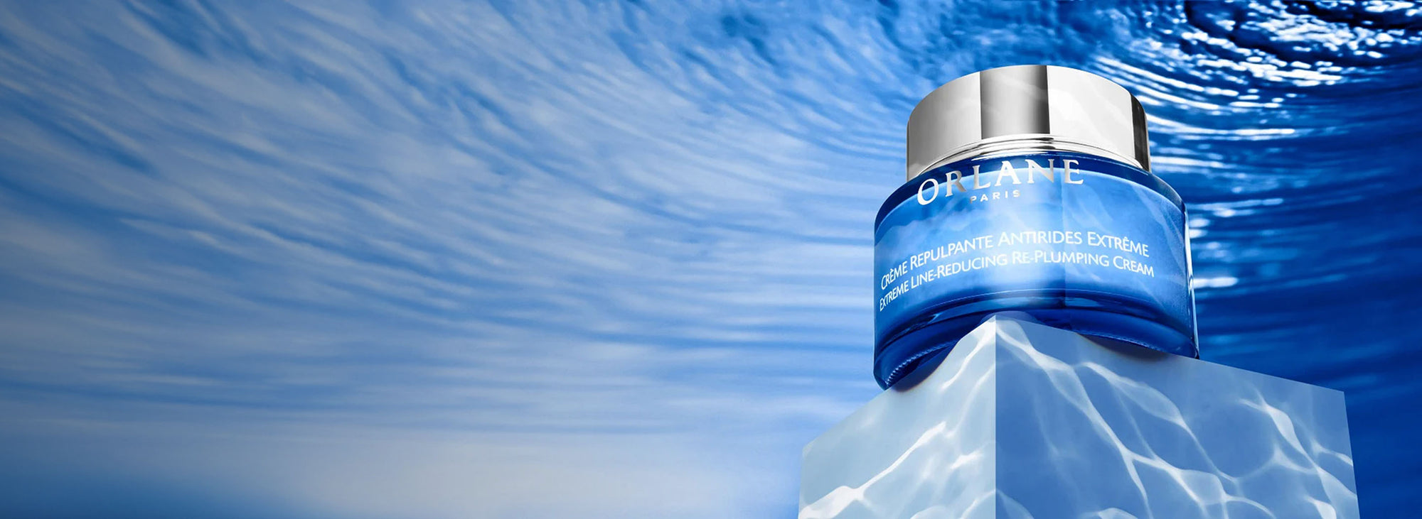 Orlane Extreme Line-Reducing Re-Plumping Cream jar displayed on a water-textured pedestal with rippling blue background