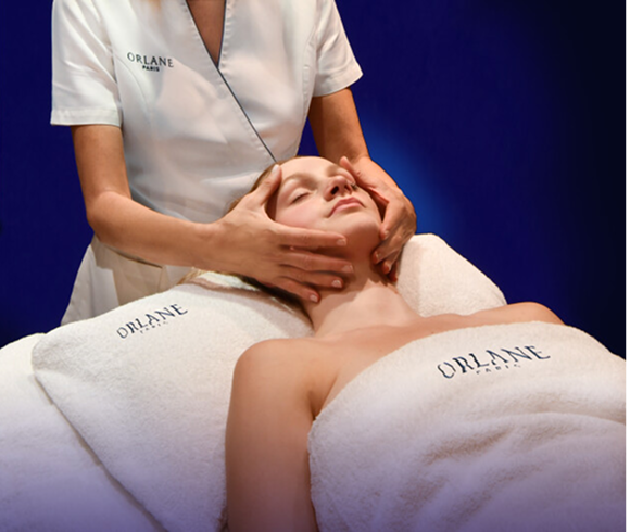 Client receiving a professional facial massage at the Orlane Institut, wrapped in branded towels and guided by an esthetician in Orlane uniform